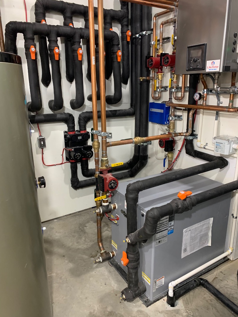 Un système de chauffage central avec conduits en métal et tuyaux isolés dans un sous-sol.